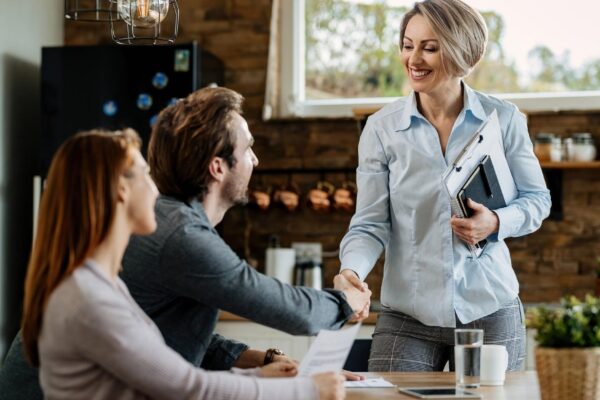 Happy insurance agent meeting with young couple and shaking hands with a man at their home