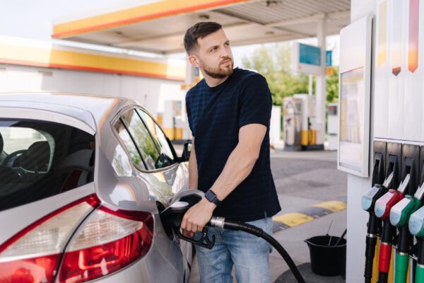 Bearded man refuelling car on gas station and looking into his smartphone man compares fuel prices