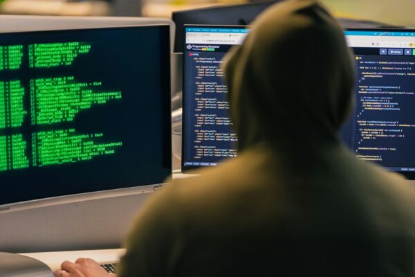 Hacker in hoodie working on multiple computer screens