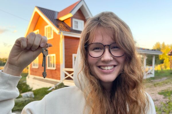 Young happy woman standing near her own house and smile at sunset