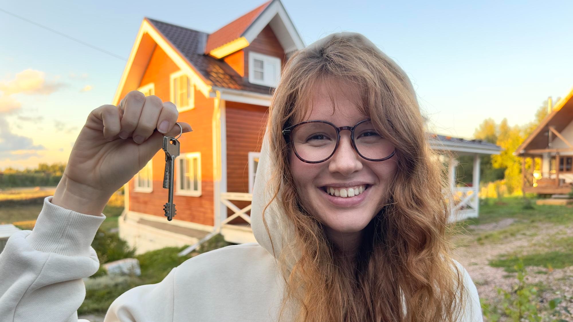 Young happy woman standing near her own house and smile at sunset