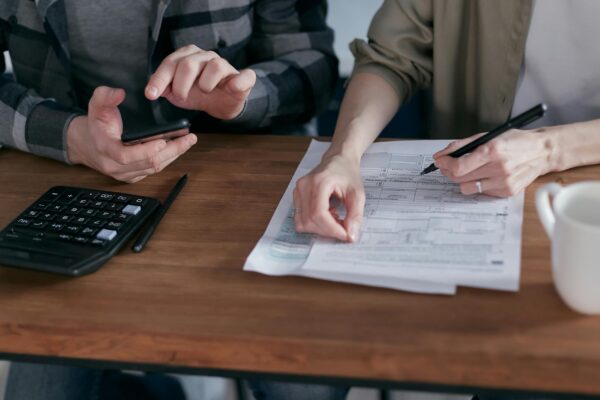 Two people working together on tax forms using a calculator at a wooden desk.
