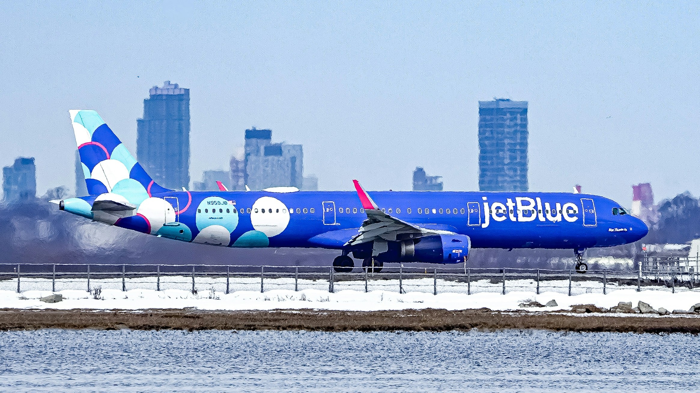 A blue jetblue airplane lands with city skyline background