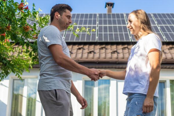 Smiling man and woman shaking hands in front of a house with solar panels Agreement