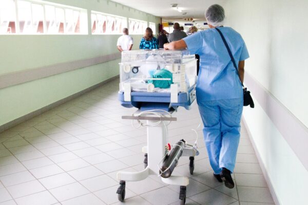 person walking on hallway in blue scrub suit near incubator