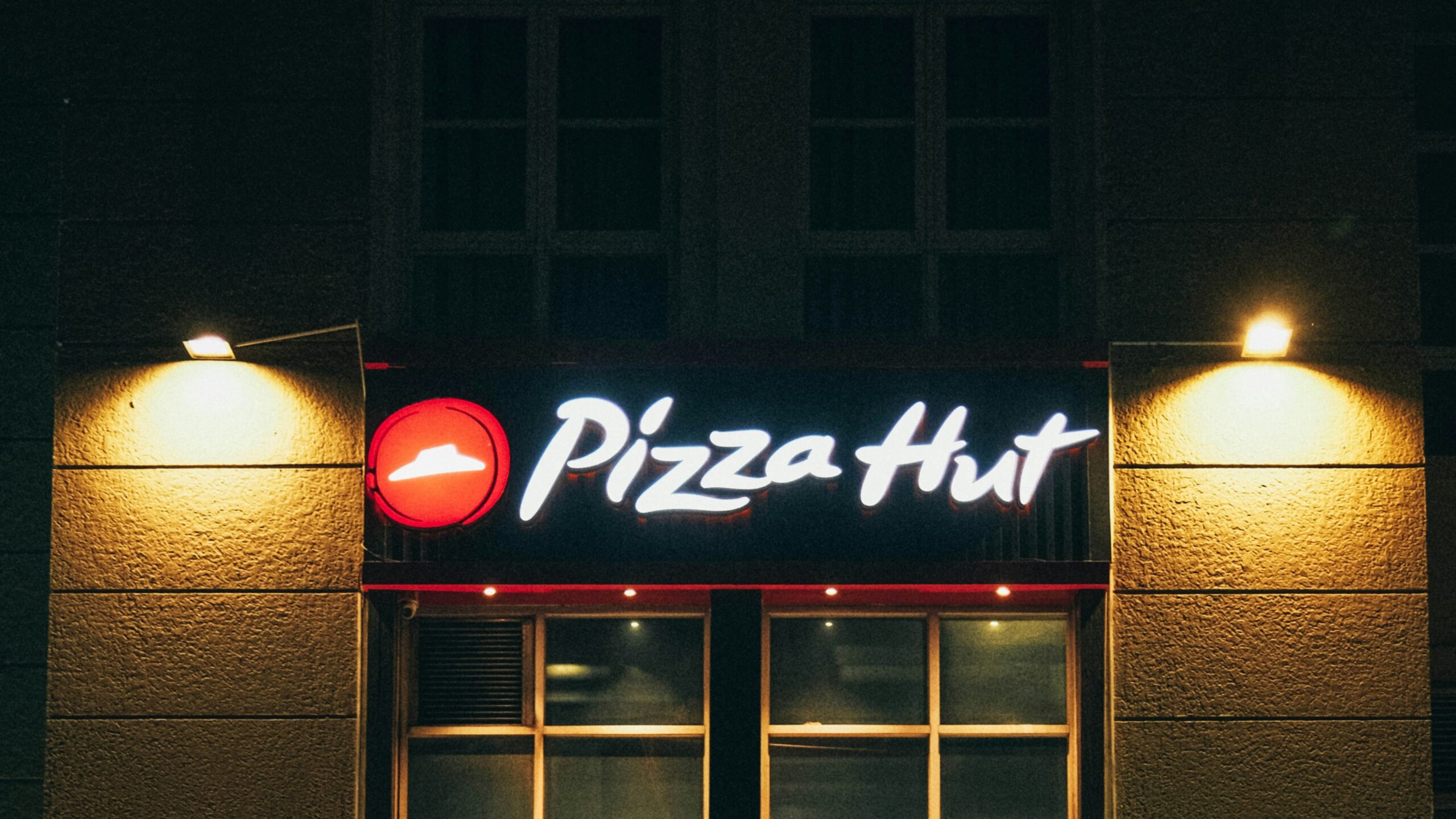 a man walking past a pizza hut at night