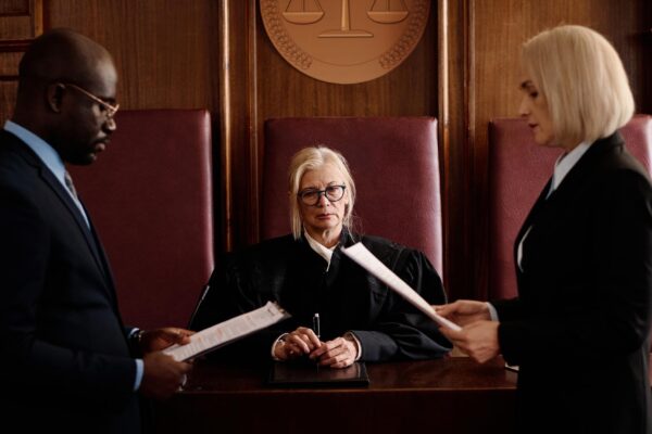 Confident mature female judge sitting by desk between prosecution and defense sides
