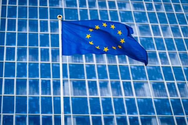 Image of EU flag fluttering on wind against high business office building made of concerete and glass. Concept of ecenomics, development, government and politics