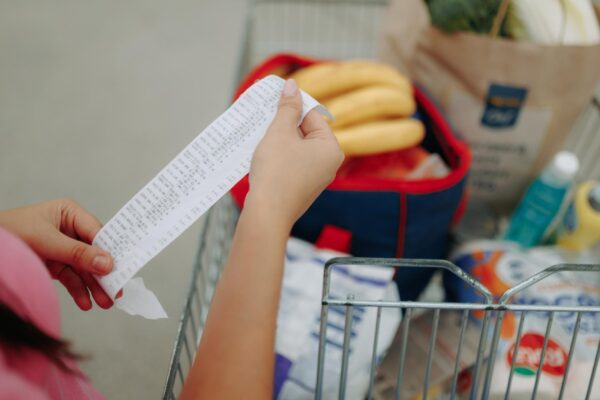 Closeup of hands holding shopping receipt near loaded cart