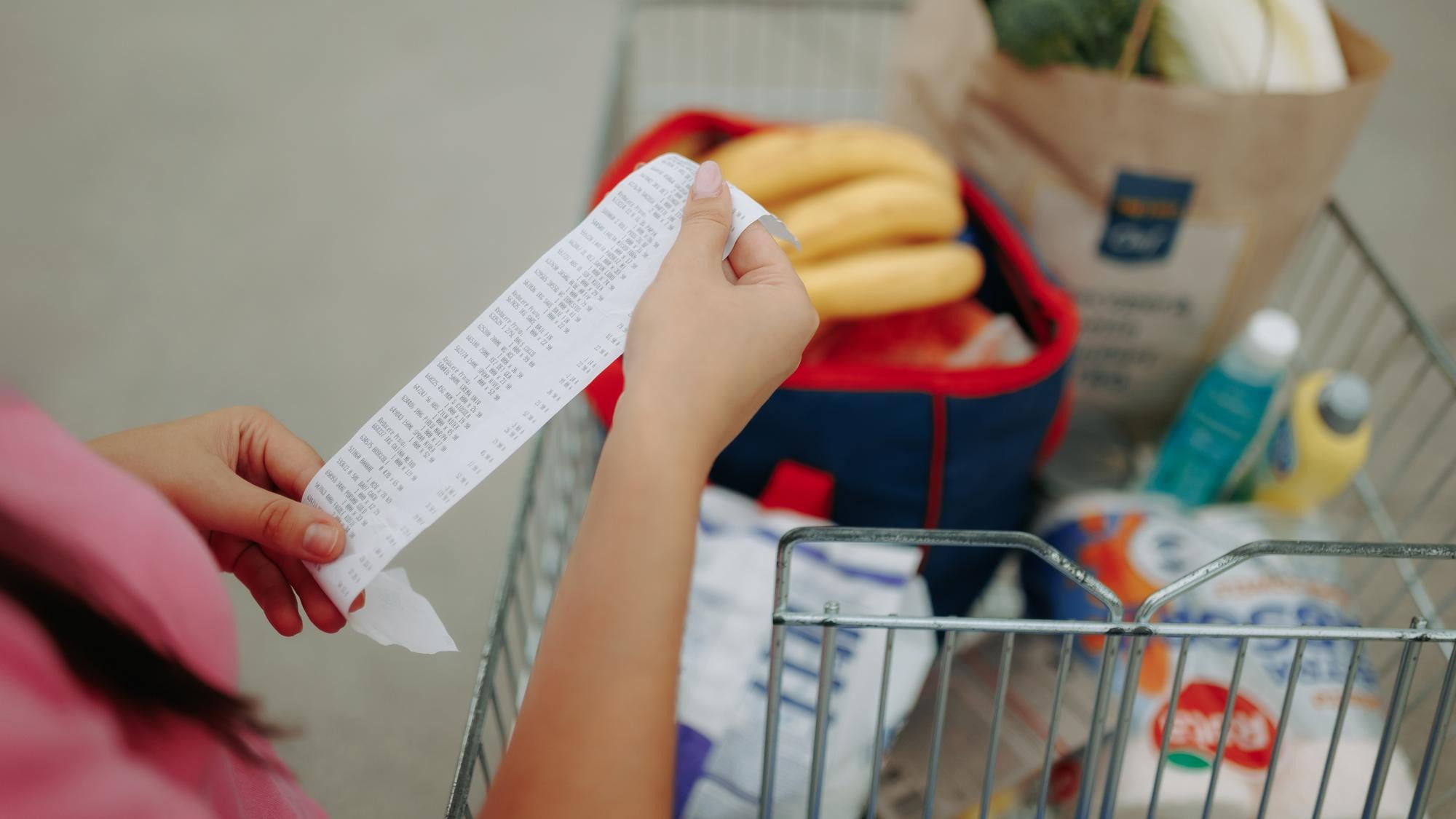 Closeup of hands holding shopping receipt near loaded cart