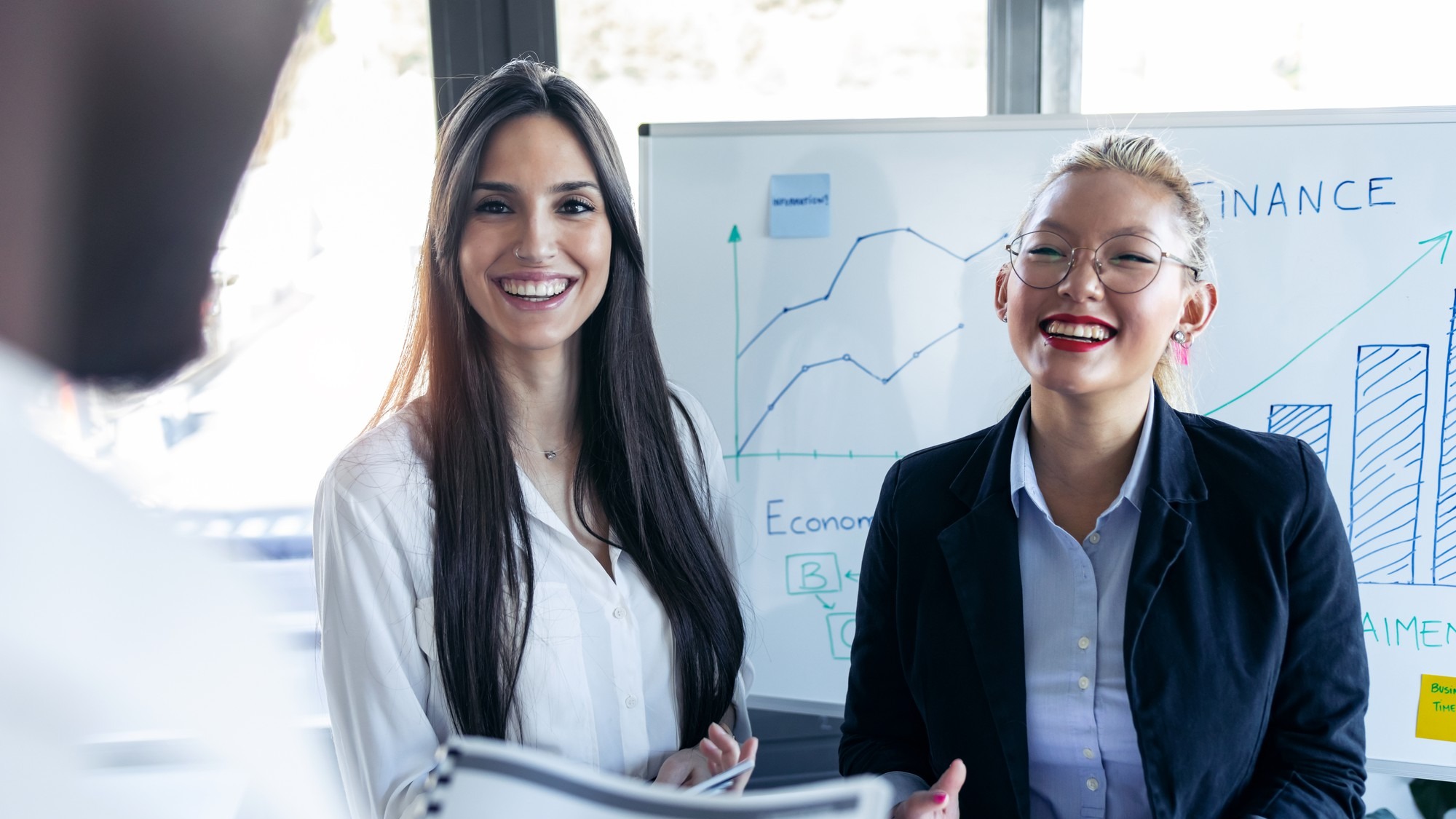 Shot of two elegant young businesswomen smiling and looking to her colleague on meeting in the coworking space.