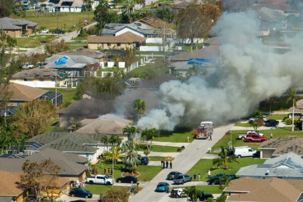 Aerial view of house on fire and firefighters extinguishing flames after short circuit caused spark to ignite wooden roof damaged by hurricane Ian wind Home disaster in Florida suburban area