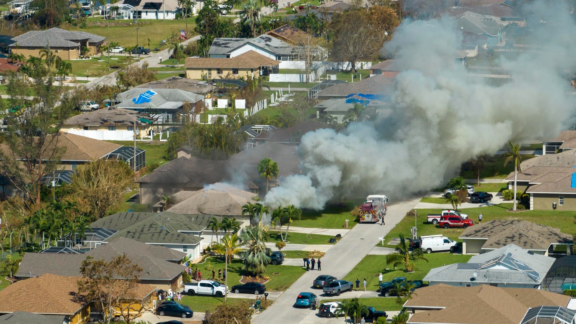 Aerial view of house on fire and firefighters extinguishing flames after short circuit caused spark to ignite wooden roof damaged by hurricane Ian wind Home disaster in Florida suburban area