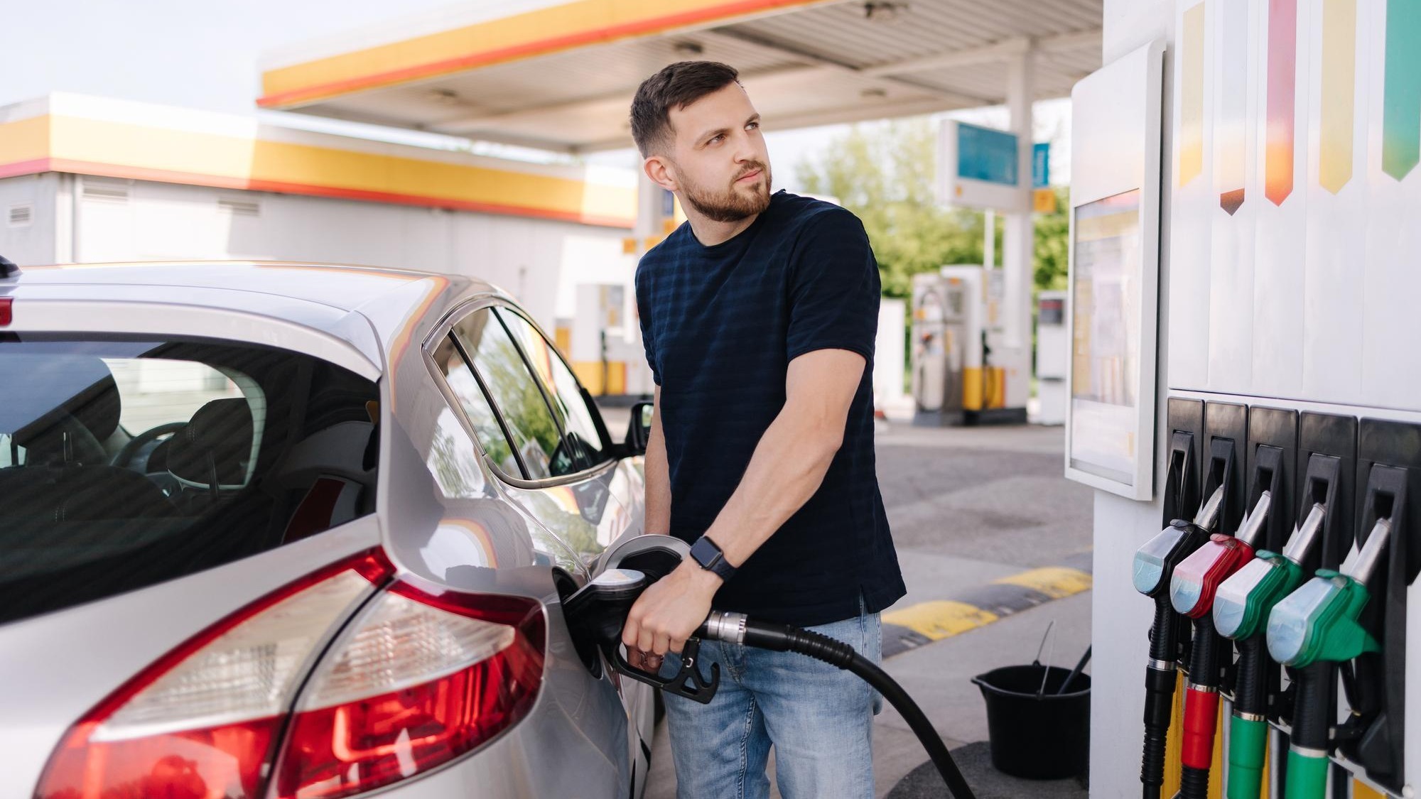 Bearded man refuelling car on gas station and looking into his smartphone man compares fuel prices
