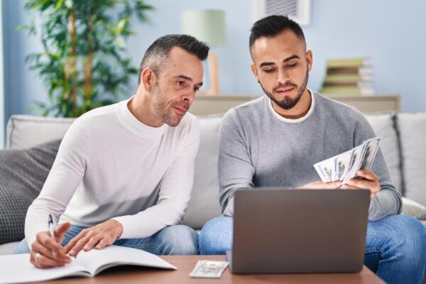 Two men writing on notebook counting dollars at home
