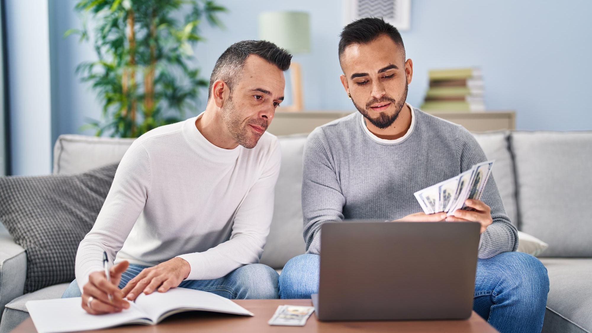 Two men writing on notebook counting dollars at home