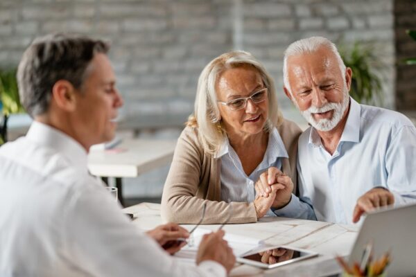 Happy senior couple holding hands and using laptop while having a meeting with financial advisor in the office Senior man is pointing at something on laptop