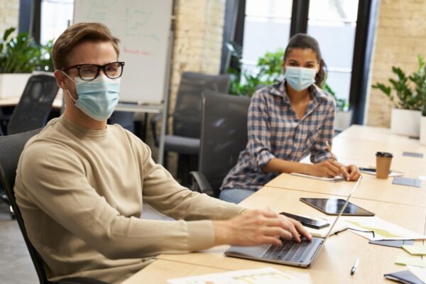 Working safely male and female office workers wearing medical protective masks sitting together at