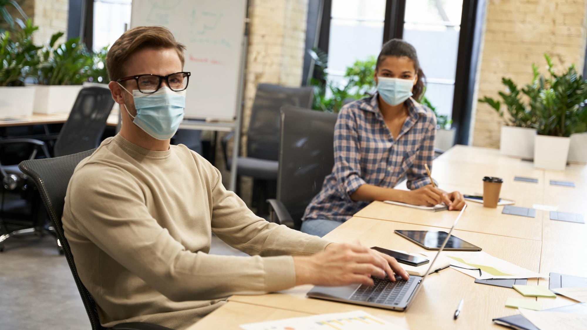 Working safely male and female office workers wearing medical protective masks sitting together at
