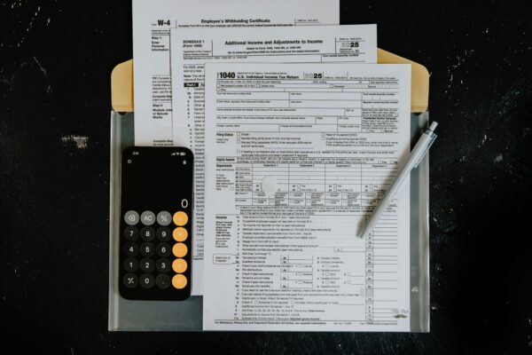 Tax forms with calculator and pen on dark surface