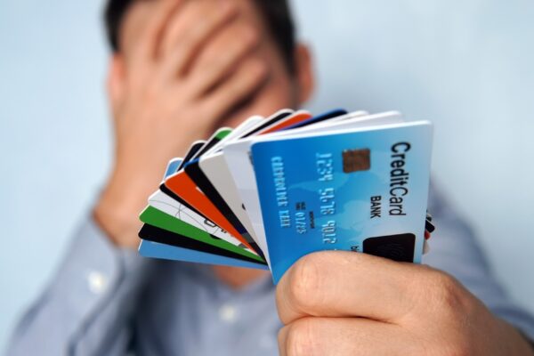 Confused man looking at many credit cards uncertain which one to choose on blue background. young man is holding a stop of credit and debit cards in a pensive pose. The guy chooses a card to pay