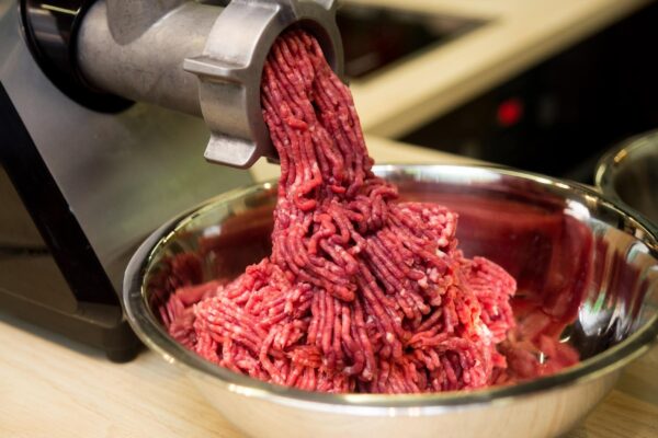 Minced meat comes out of the mincer in a metal bowl