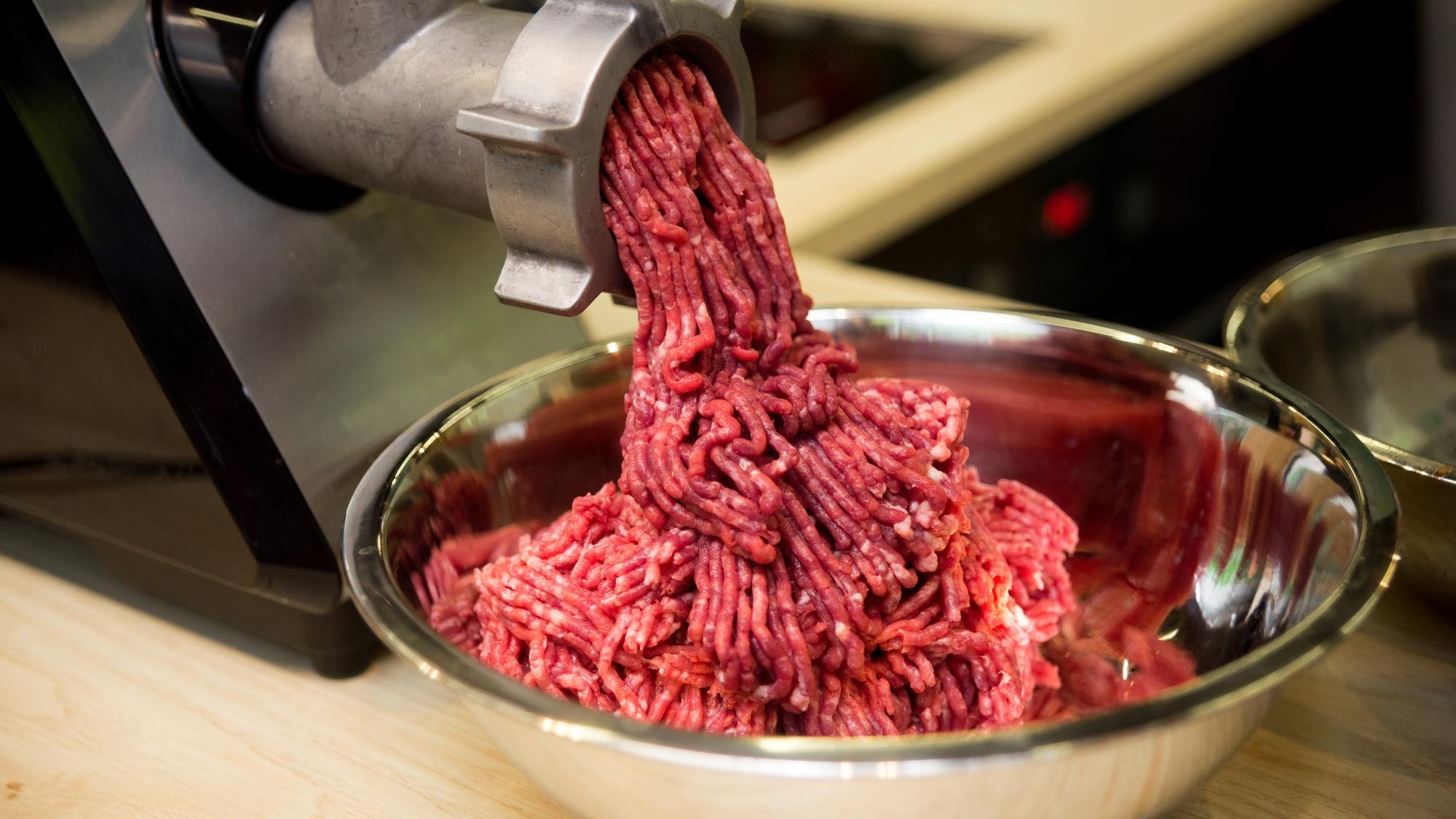 Minced meat comes out of the mincer in a metal bowl