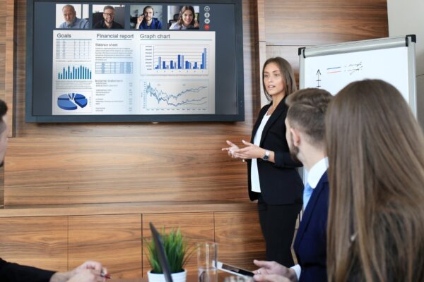 Business team at office, businessman presenting and discussing successful financial report of their company, on screen of plasma TV at meeting room, talking to his colleagues in video conference.