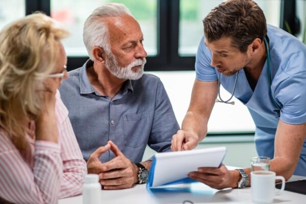 Serious doctor discussing with senior couple about their medical documents during appointment at clinic