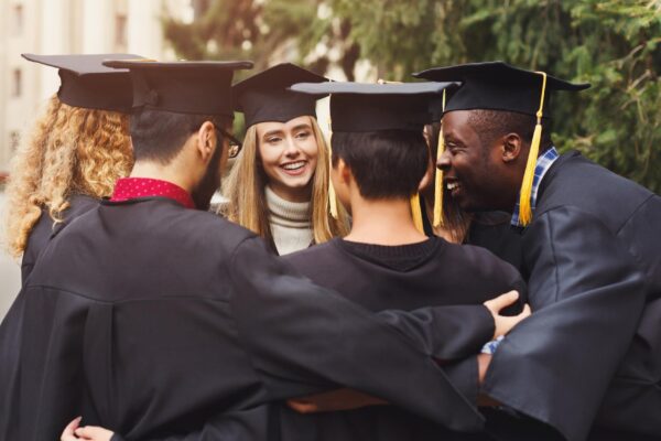 Group of multietnic students hugging on their graduation day at university, copy space. Education, qualification and gown concept.
