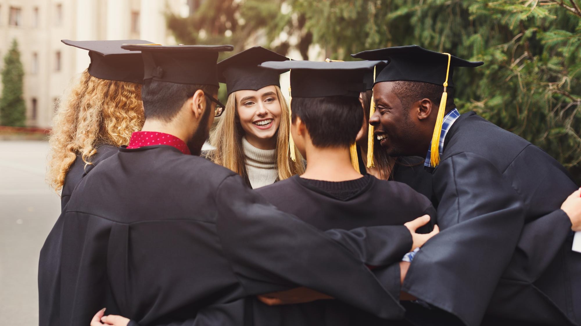 Group of multietnic students hugging on their graduation day at university, copy space. Education, qualification and gown concept.