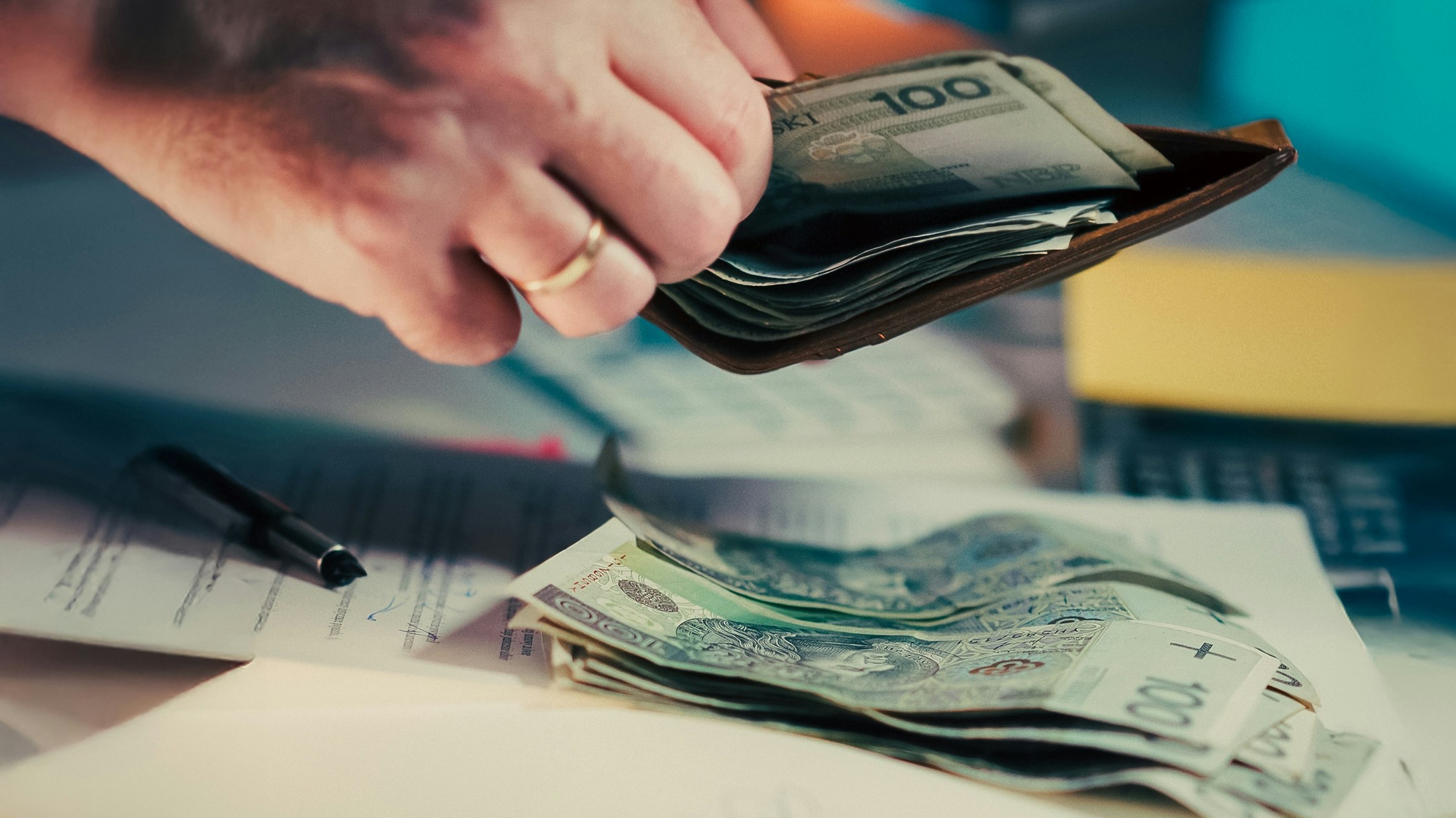Hands counting money from a wallet over papers.