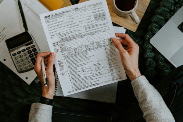 Hands holding tax forms with calculator and laptop.
