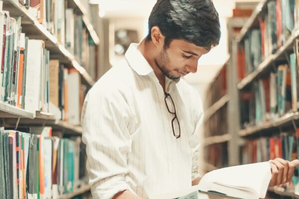 man holding and reading book while standing inside library
