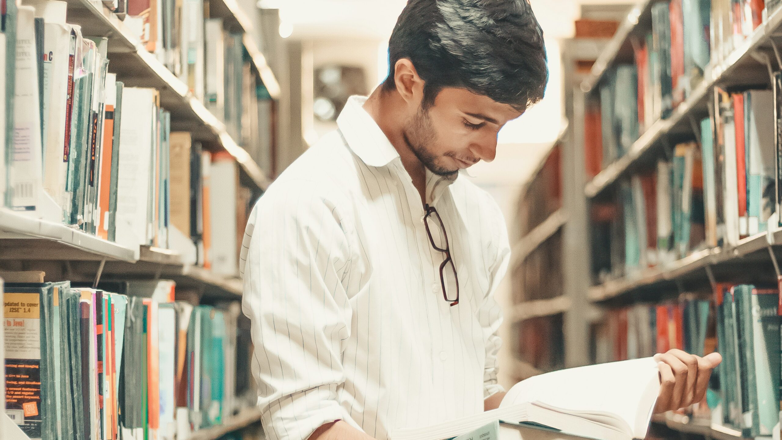 man holding and reading book while standing inside library