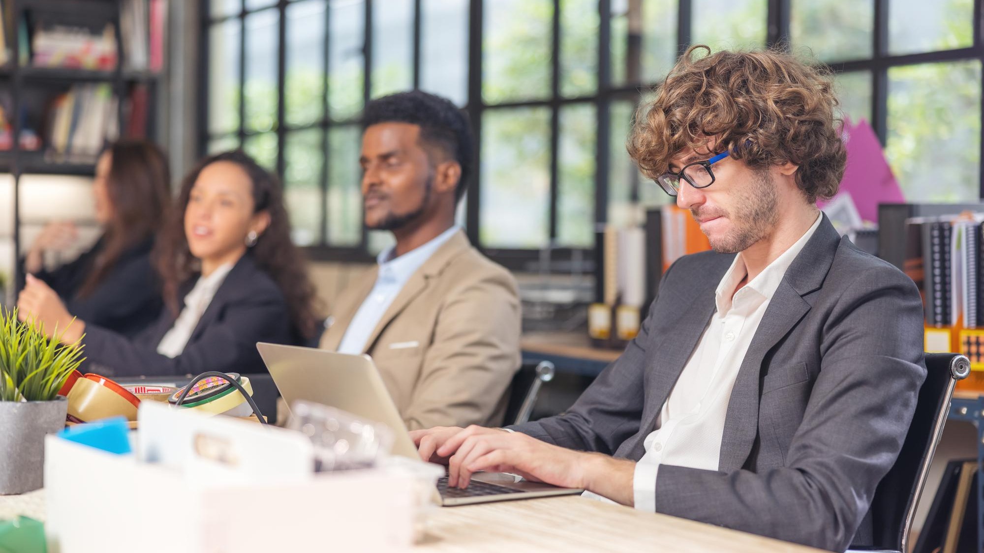 Colleagues in a boardroom discussion, seated at a table together, swapping ideas and strategizing project strategy. In the office, young business professionals