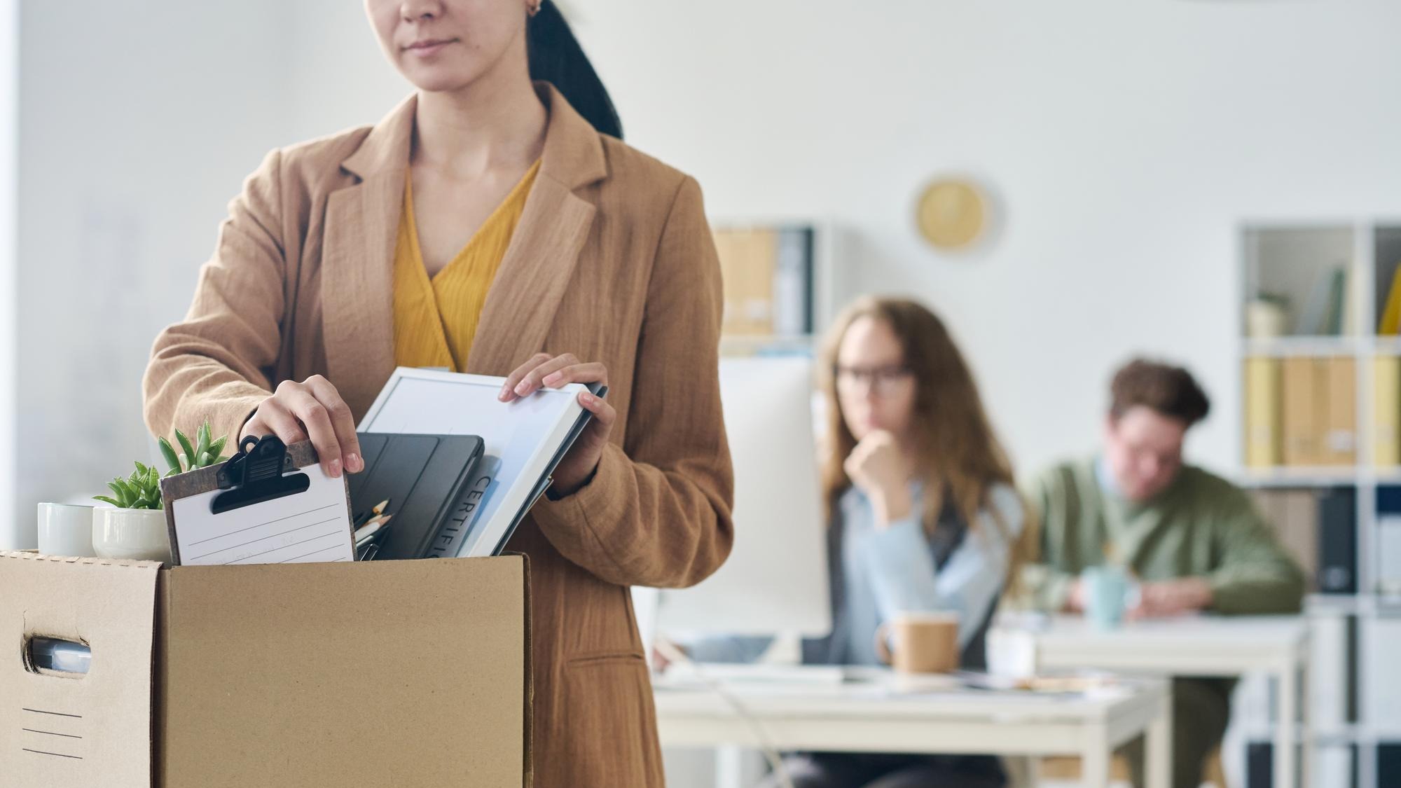 Young businesswoman packing her things in cardboard box in office after her layoff