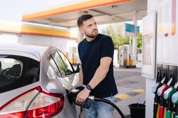 Bearded man refuelling car on gas station and looking into his smartphone man compares fuel prices