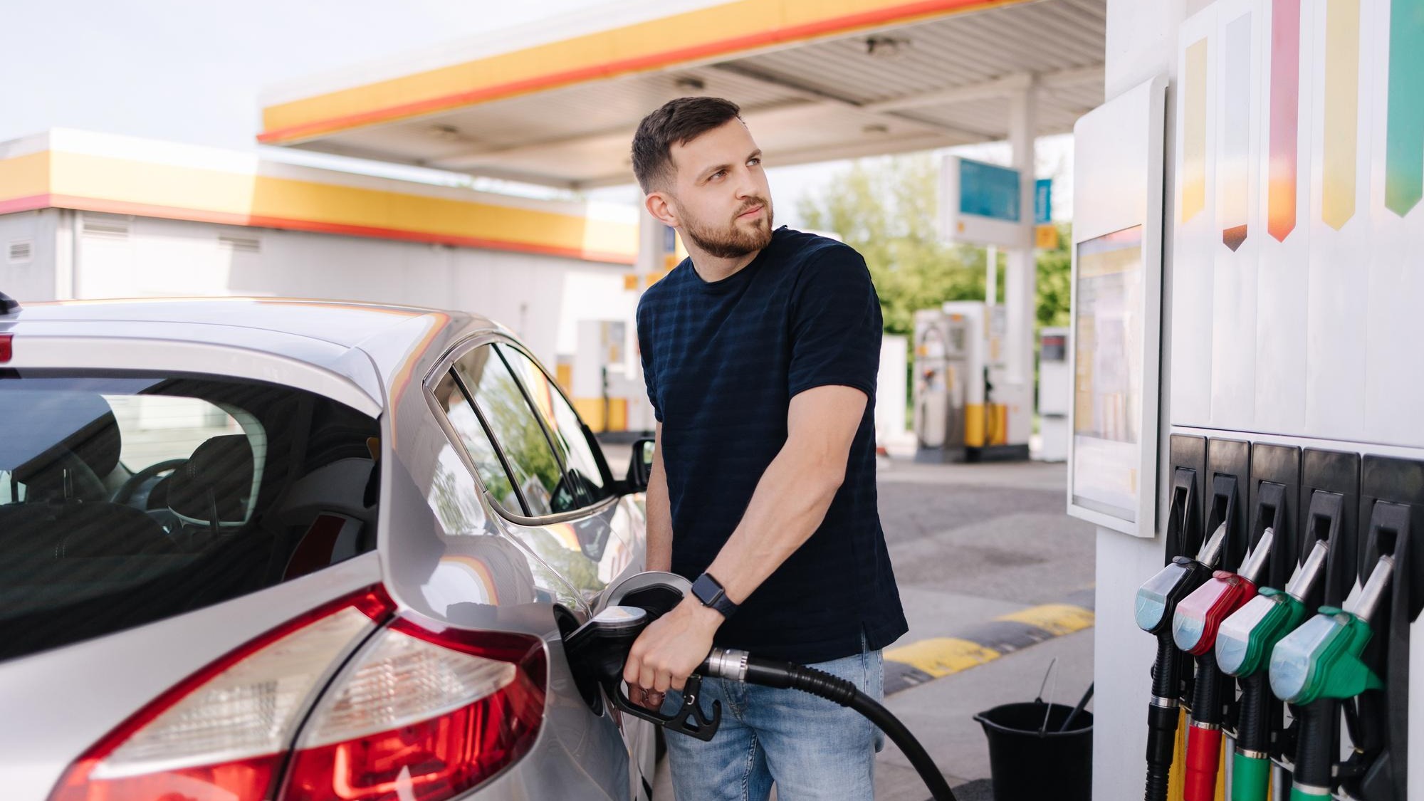 Bearded man refuelling car on gas station and looking into his smartphone man compares fuel prices