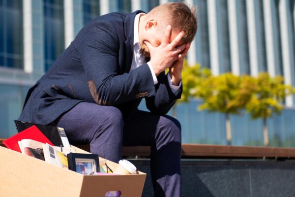 Depleated former employee sitting with his belongings stuffed in a box next to him