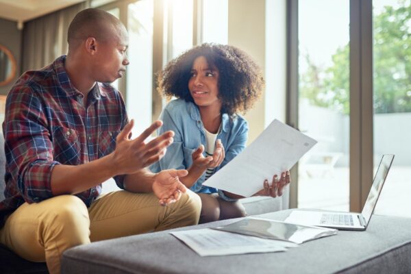 Financial paperwork planning or couple with questions finance documents or budget in home Receipt laptop or worried people speaking of bills doubt or debt with recession taxes or inflation