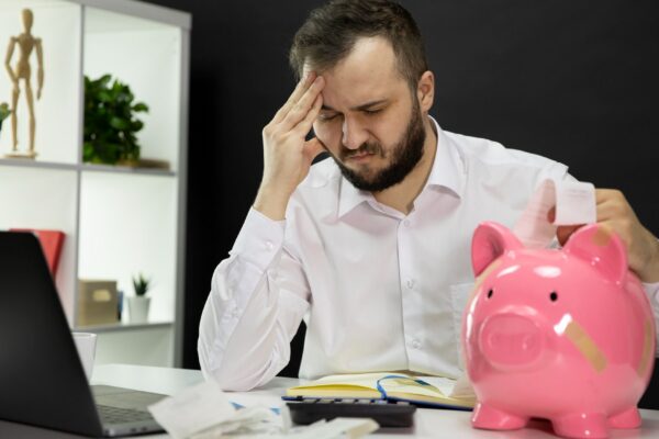 Man in despair looking on bills with broken piggy bank in foreground, Bankruptcy