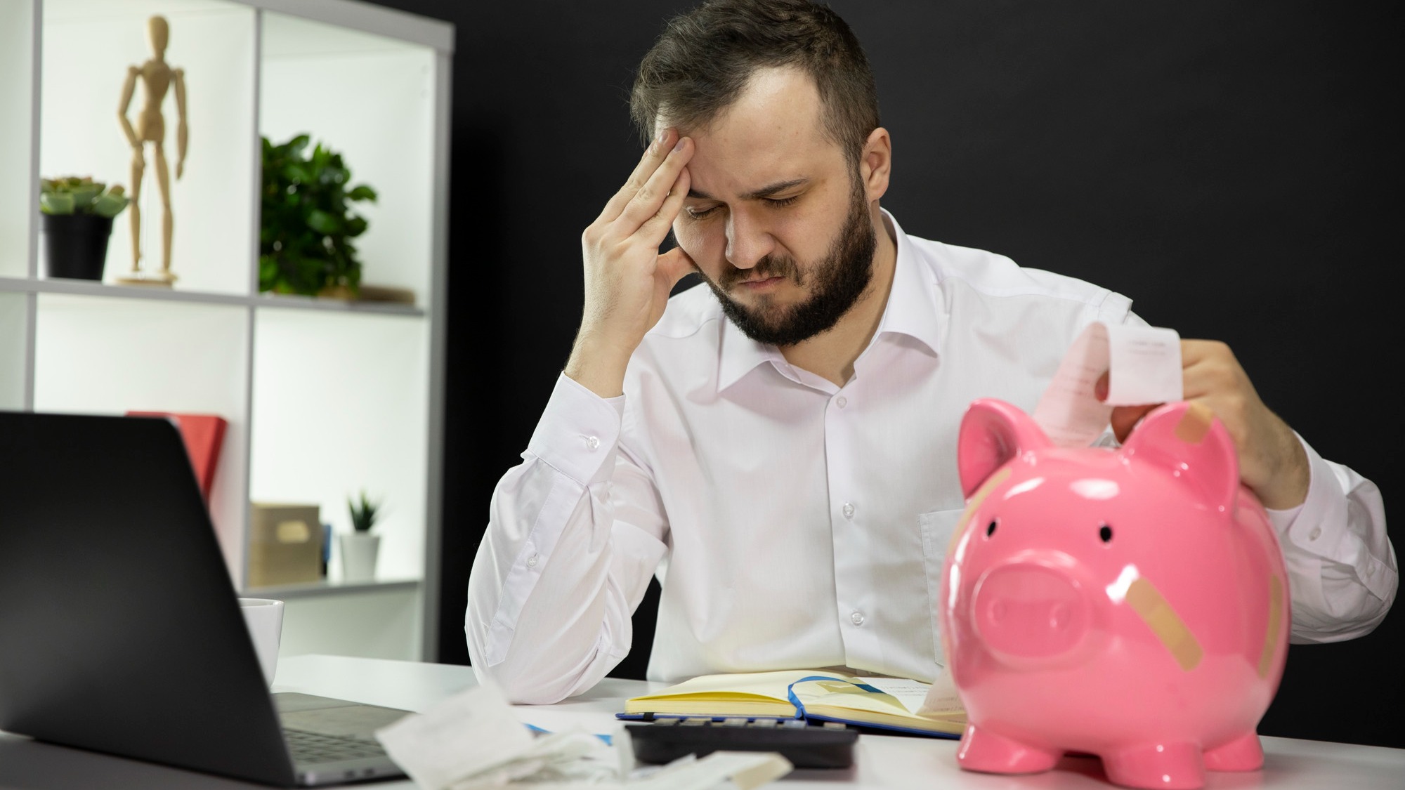 Man in despair looking on bills with broken piggy bank in foreground, Bankruptcy
