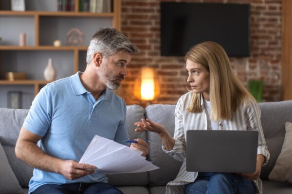 Serious mature caucasian husband and wife work with documents and laptop pay taxes