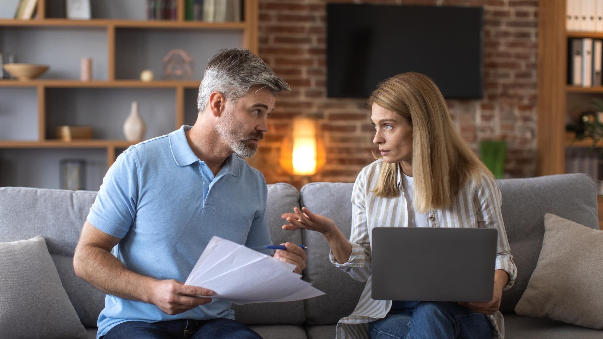 Serious mature caucasian husband and wife work with documents and laptop pay taxes