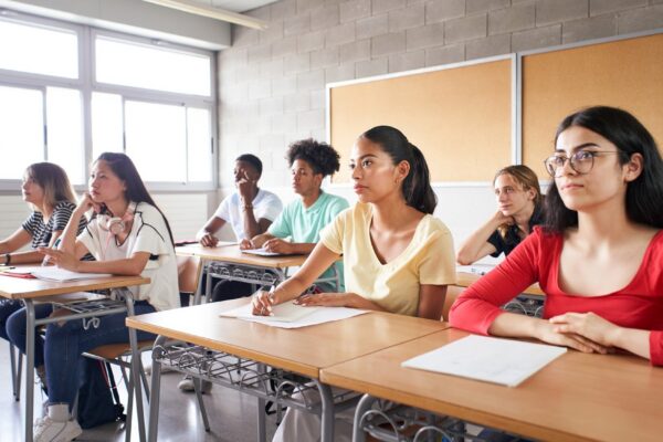 Group of students of different ethnicities sitting in class attending to the teacher young people