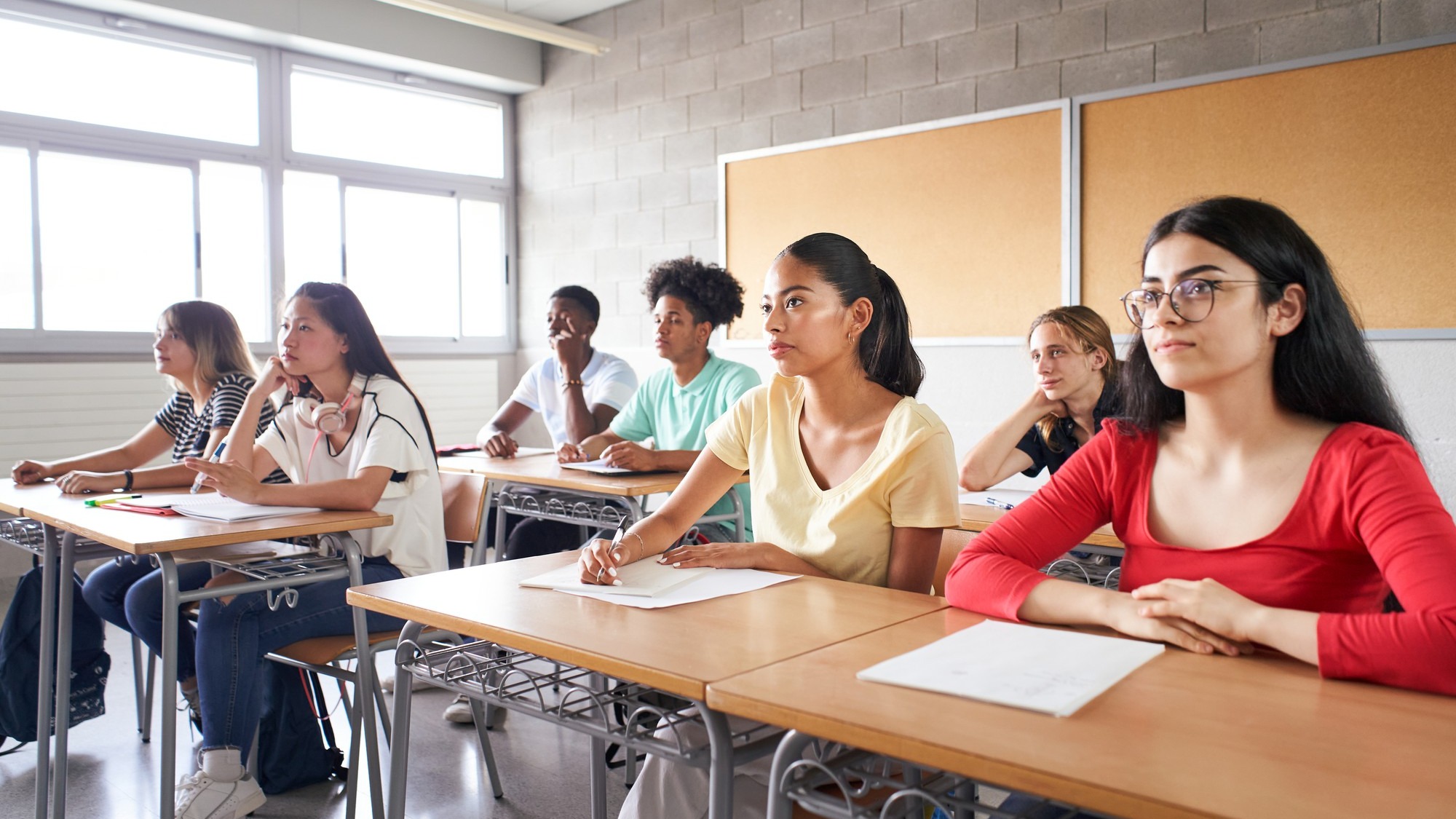 Group of students of different ethnicities sitting in class attending to the teacher young people