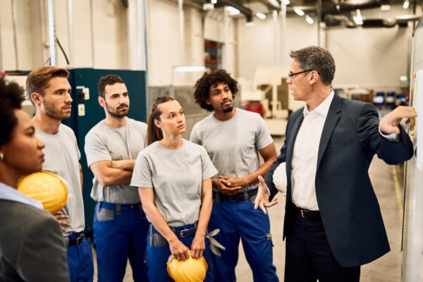Mid adult businessman giving presentation to group of industrial workers in a factory