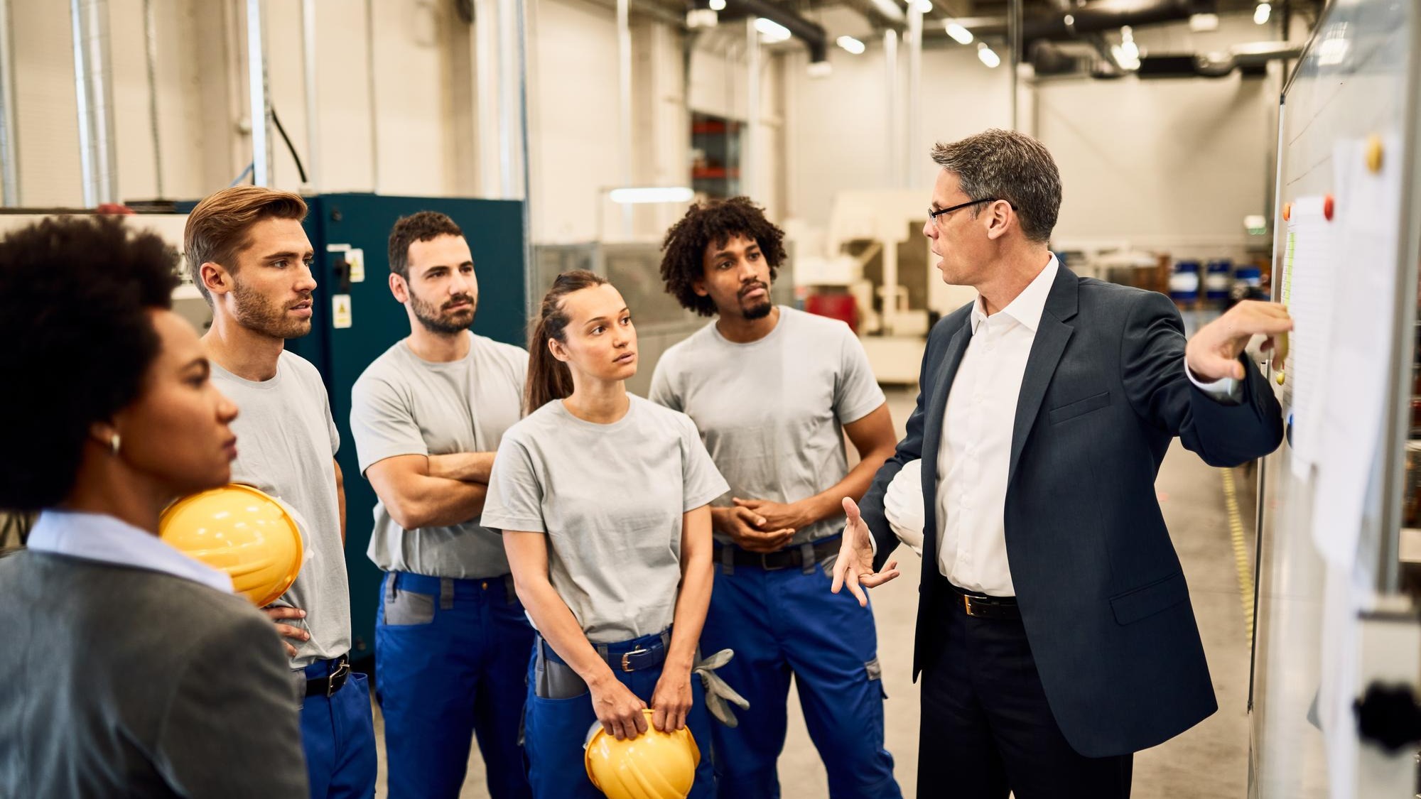 Mid adult businessman giving presentation to group of industrial workers in a factory