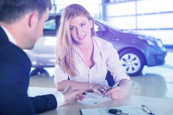 Happy woman with car dealer in auto show or salon